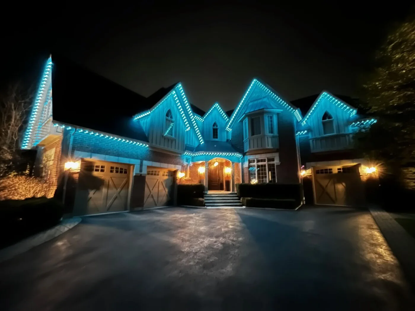 Large luxury home with teal permanent LED roofline lighting at night