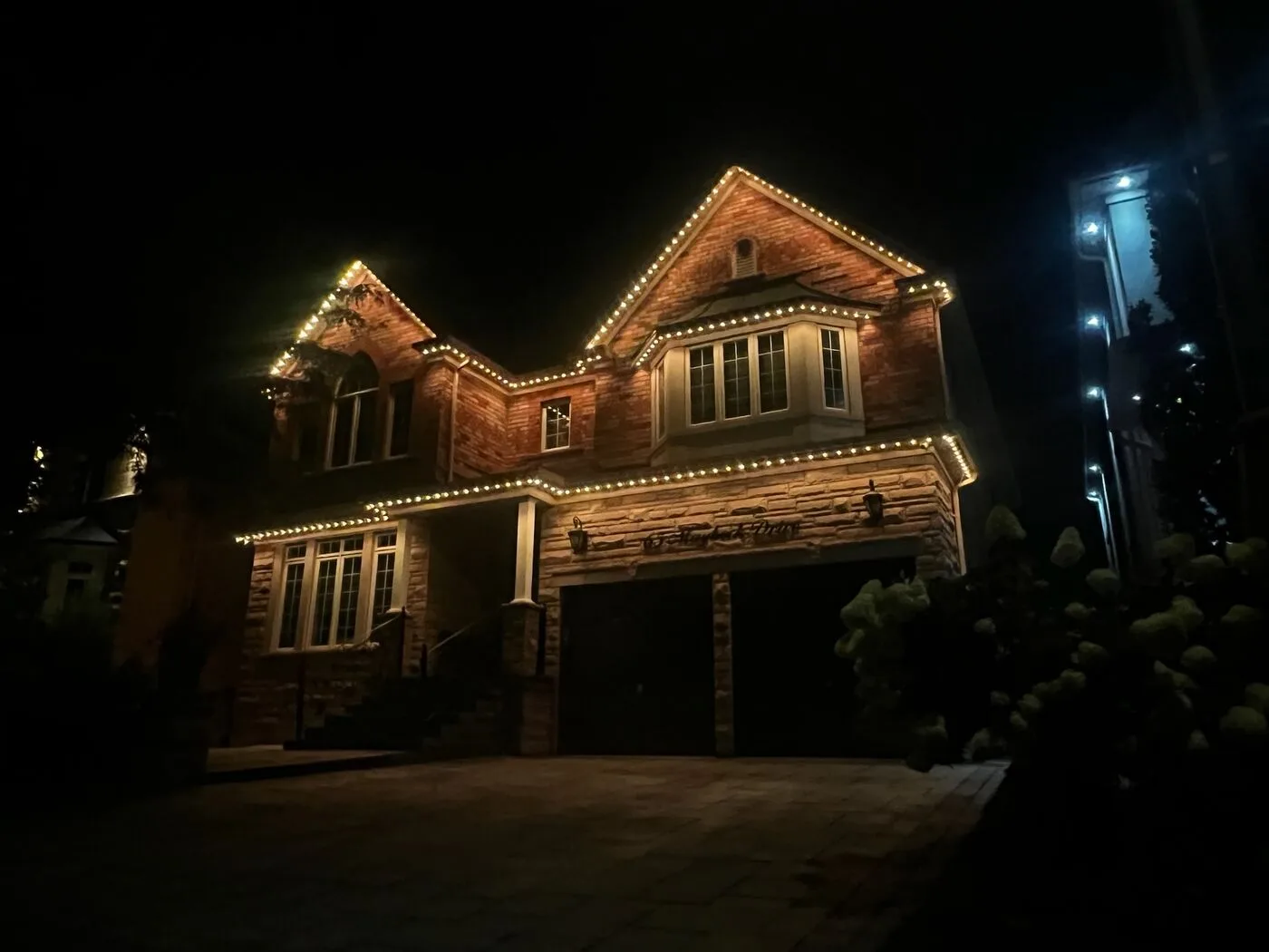Stone home with warm white permanent LED roofline lighting at night