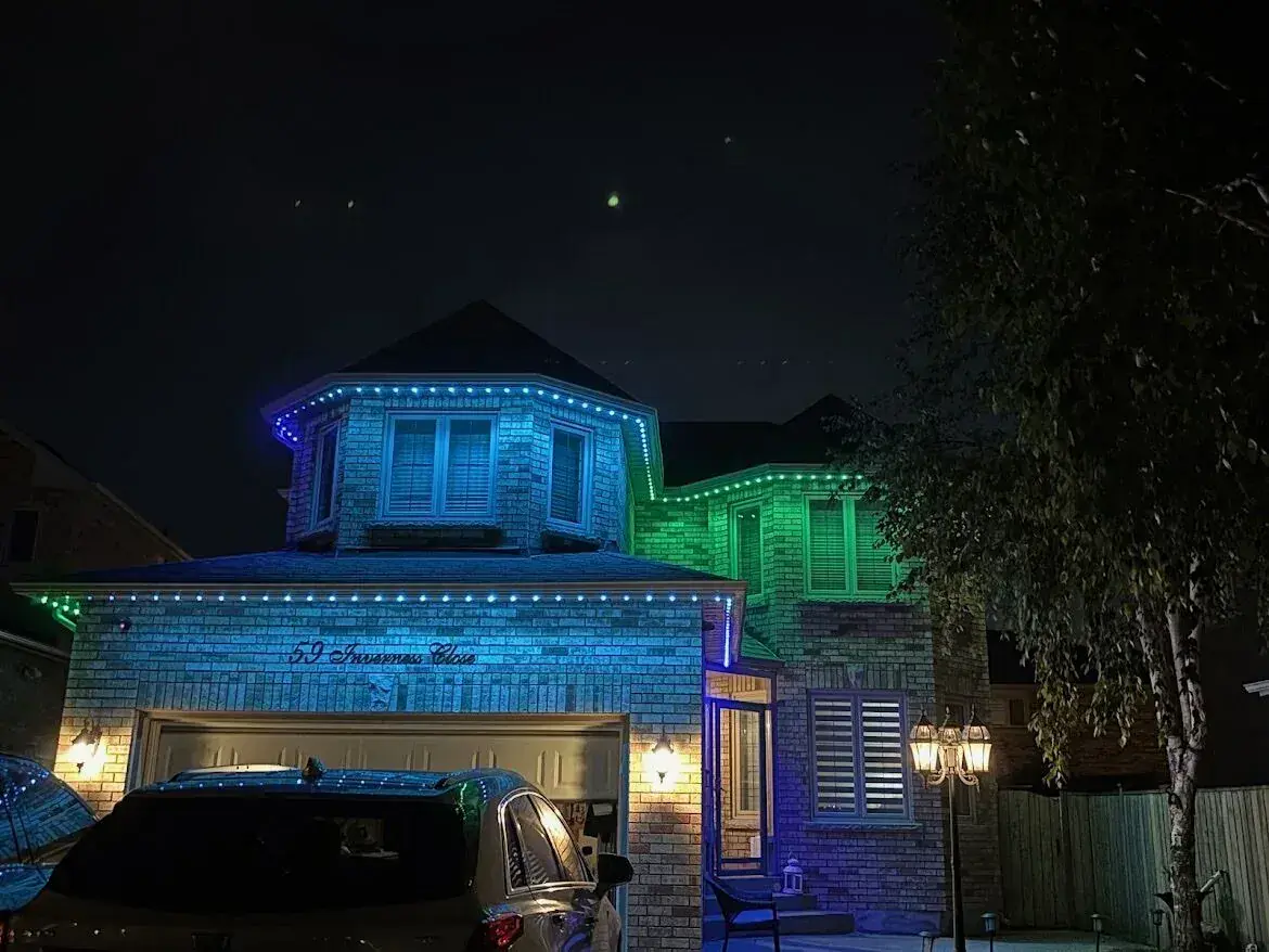 Brick home with blue and green permanent LED roofline lighting at night