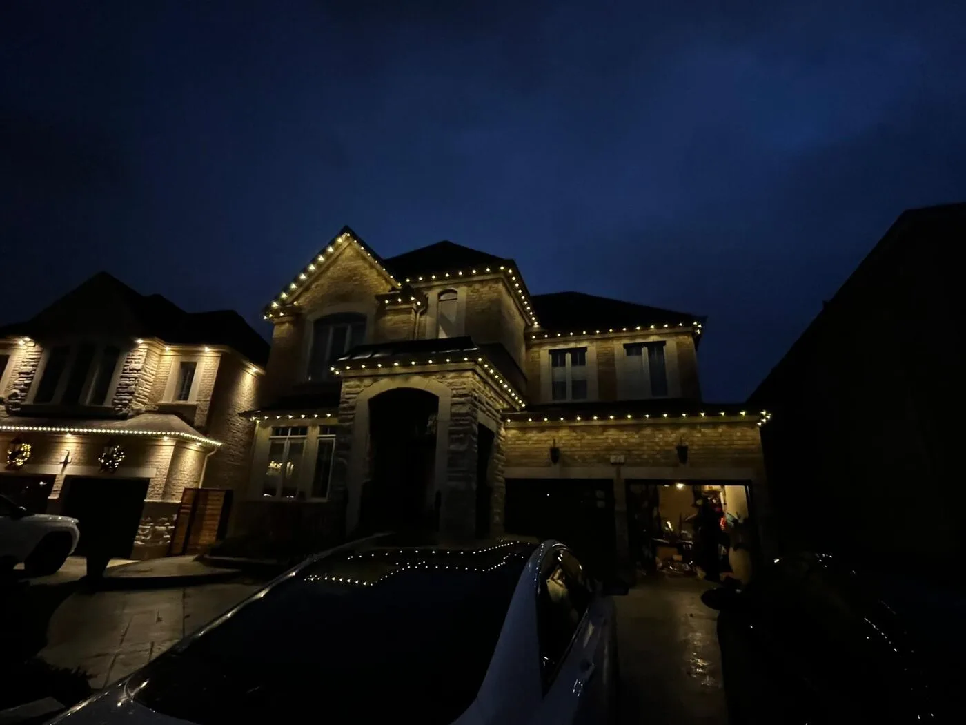 Large stone home with warm white permanent LED roofline lighting at dusk