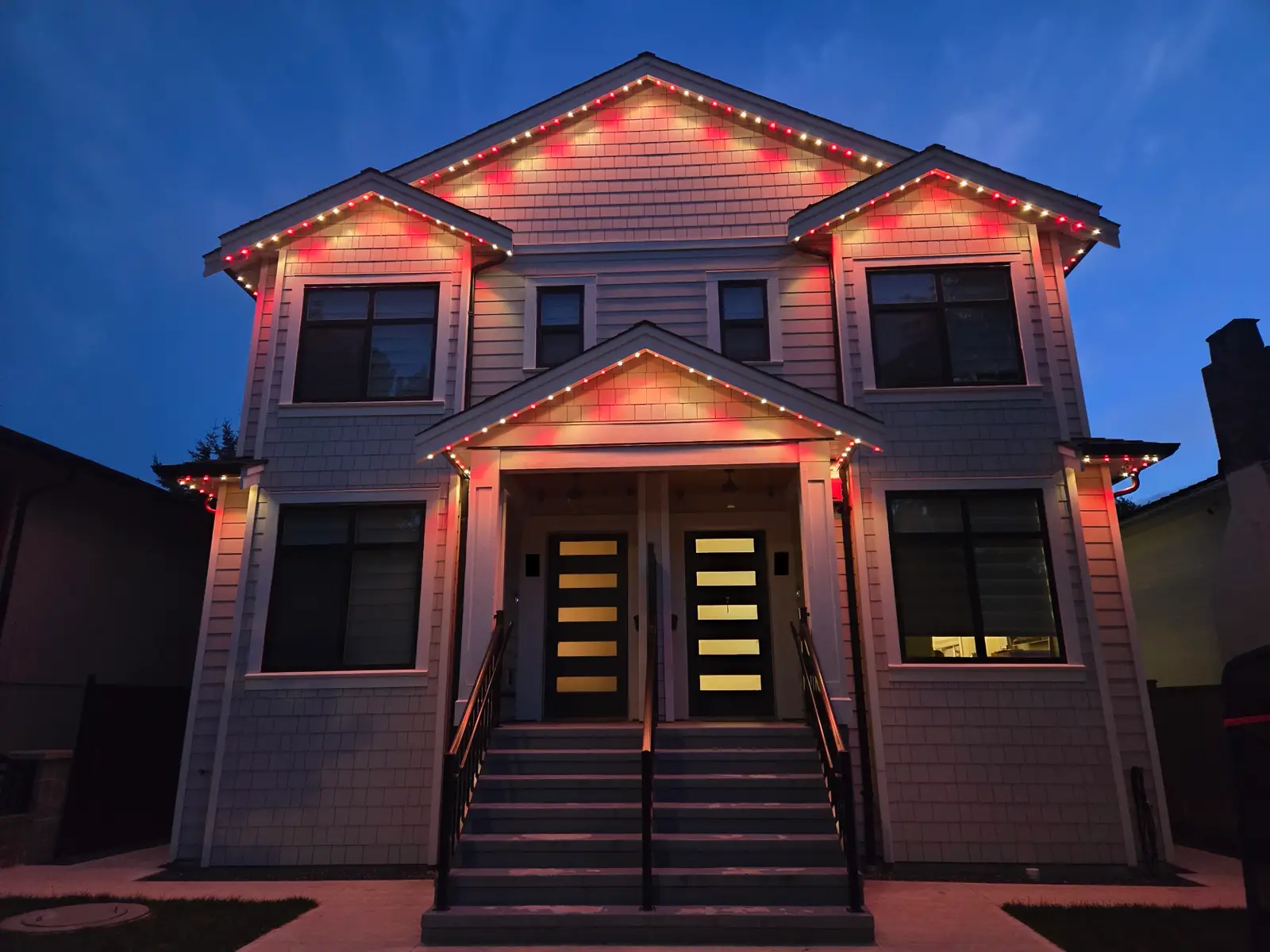 Modern duplex with pink and red permanent LED roofline lighting at dusk in Vancouver